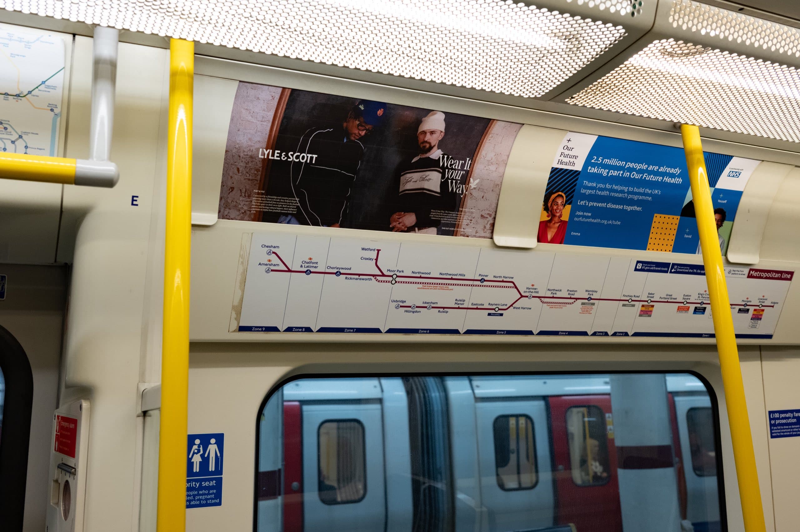 A second Lyle & Scott tube car panel execution photographed against a brick backdrop, running above the Metropolitan line diagram in a carriage.