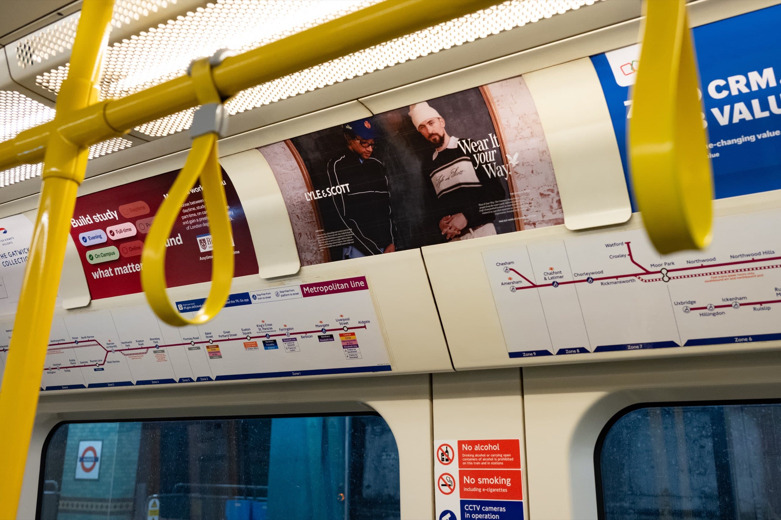 A Lyle & Scott tube car panel seen along the length of a Metropolitan line carriage, with grab handles in the foreground and the line diagram below.