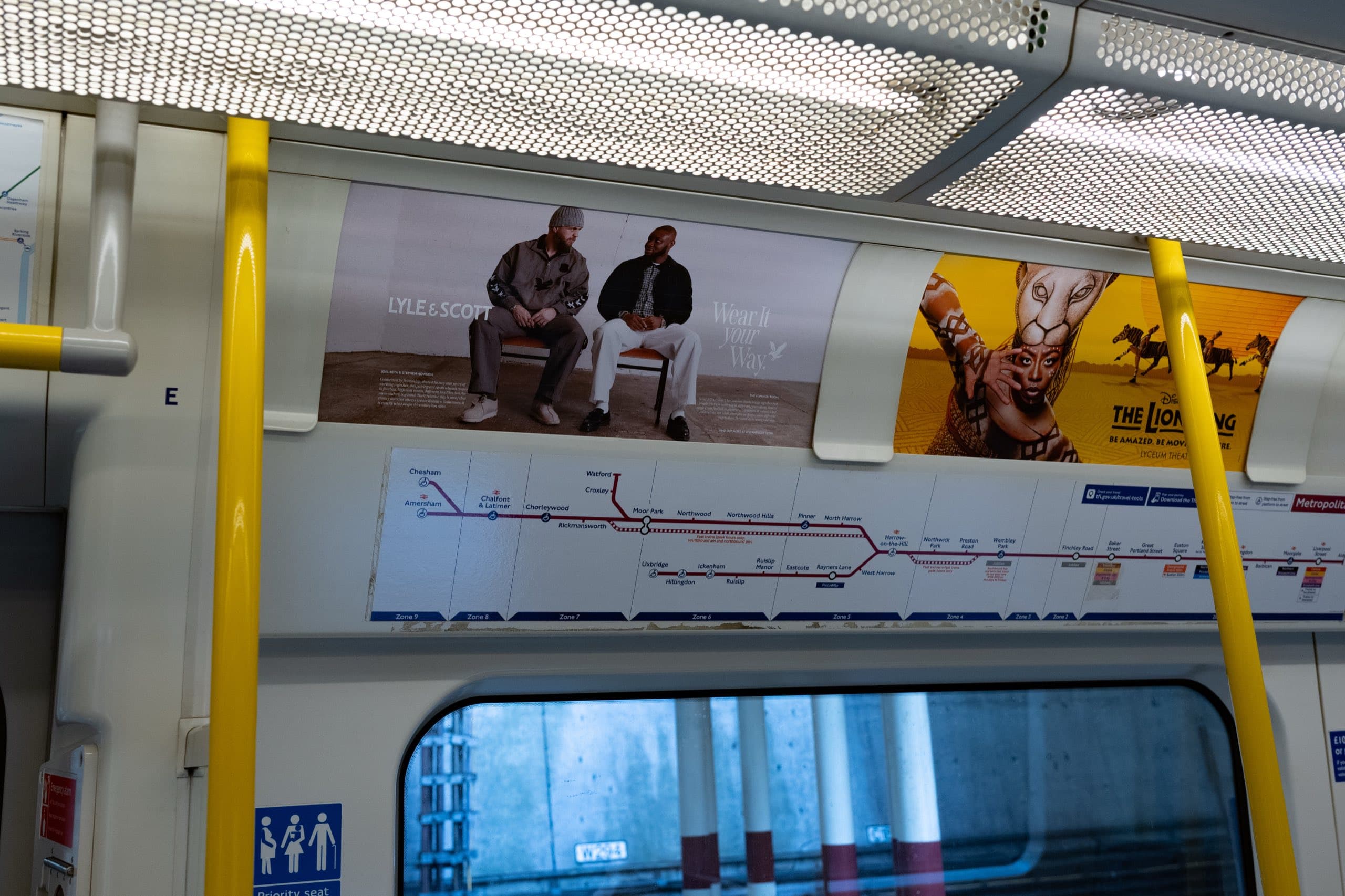 A Lyle & Scott “Wear It Your Way” tube car panel above the Metropolitan line diagram inside a carriage, showing two men seated on a bench.