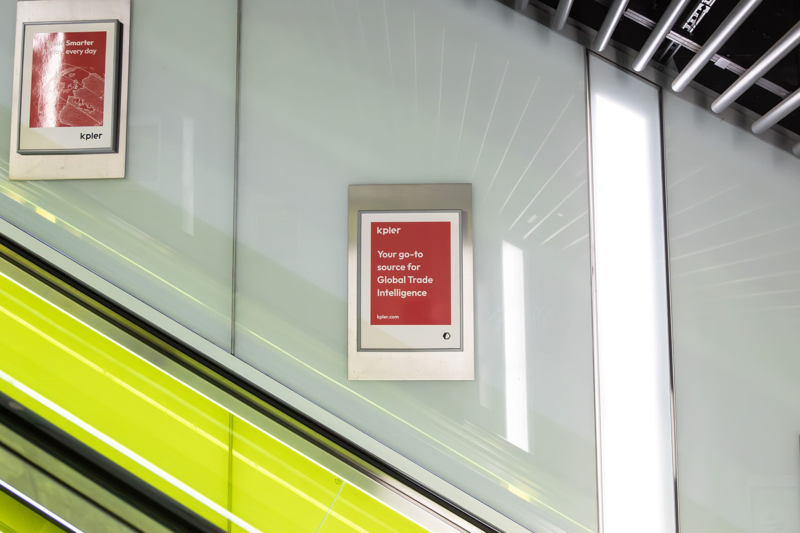 Static escalator panels carrying Kpler advertisements alongside a glass-sided Underground escalator.
