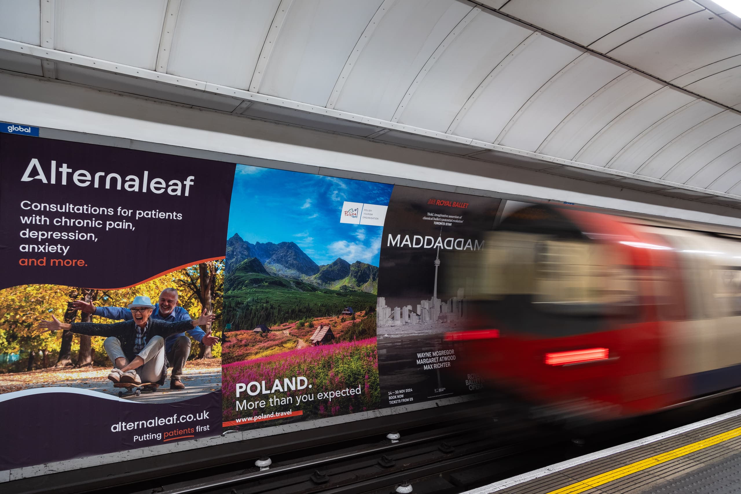 A run of cross-track posters at Tottenham Court Road including a Polish Tourism Organisation advertisement, with a train passing at speed.
