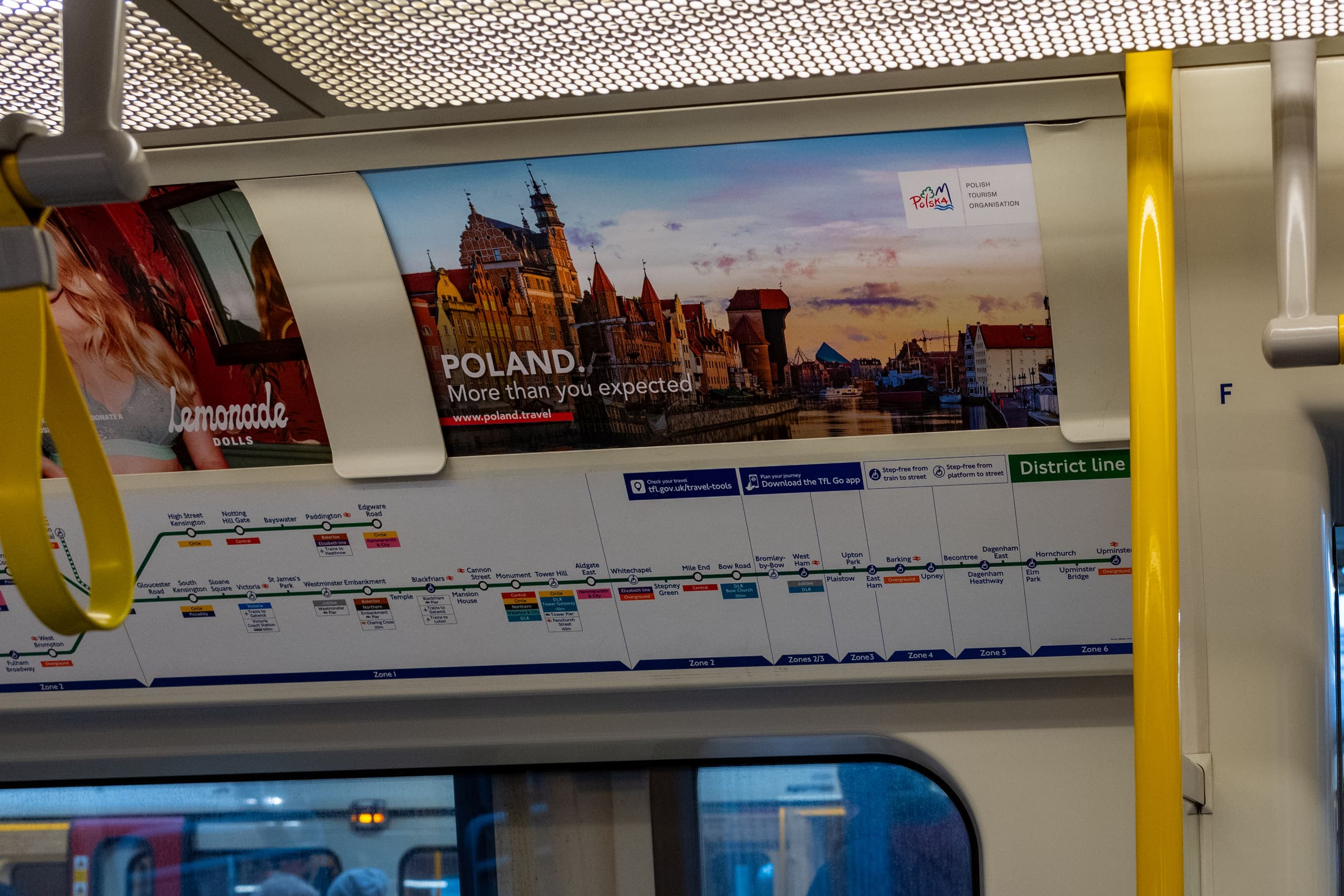 A landscape tube car panel above the windows of a District line carriage, carrying a Polish Tourism Organisation advertisement.