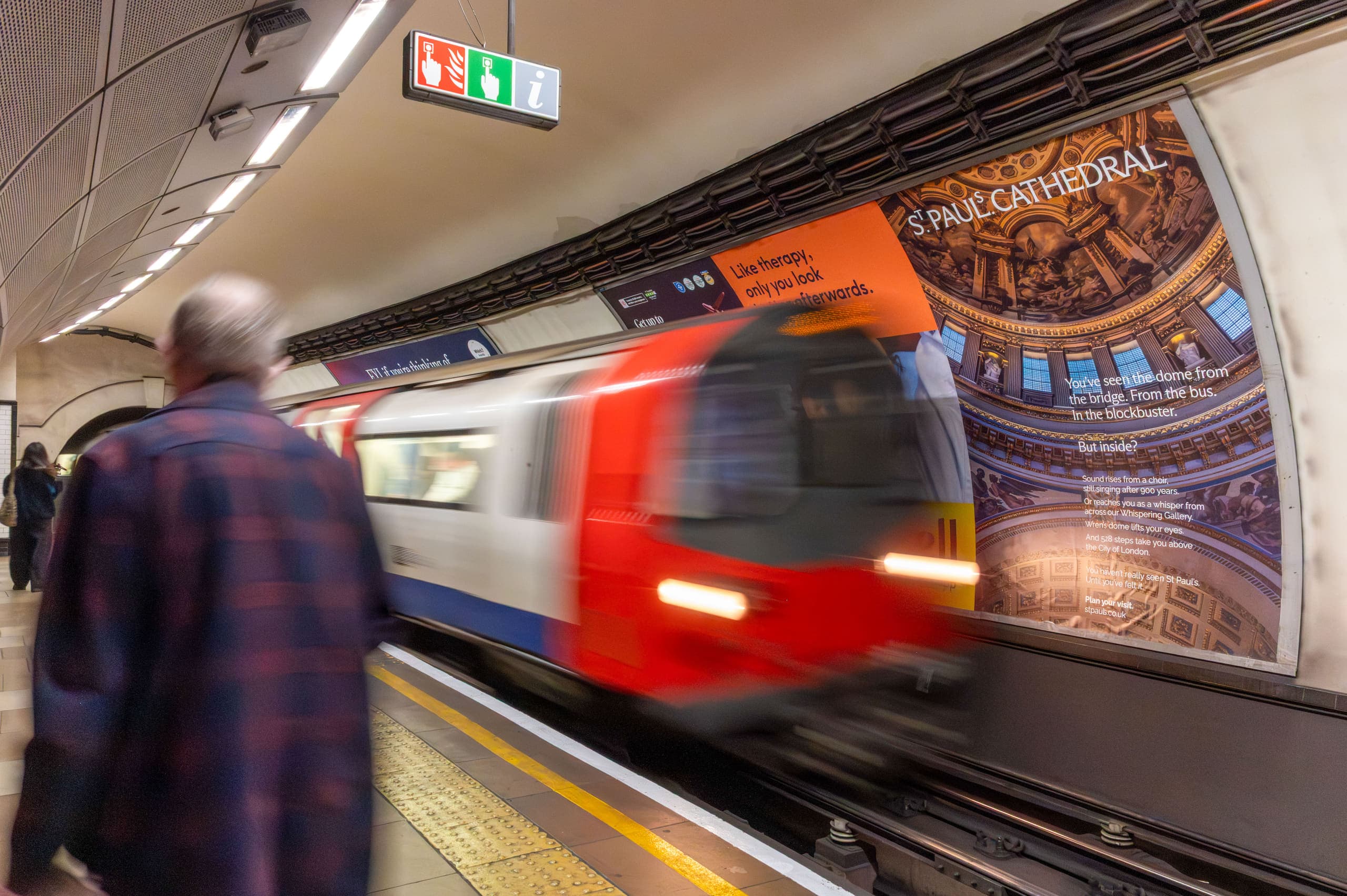 A large cross-track poster advertising St Paul's Cathedral on the platform wall, with a train passing.