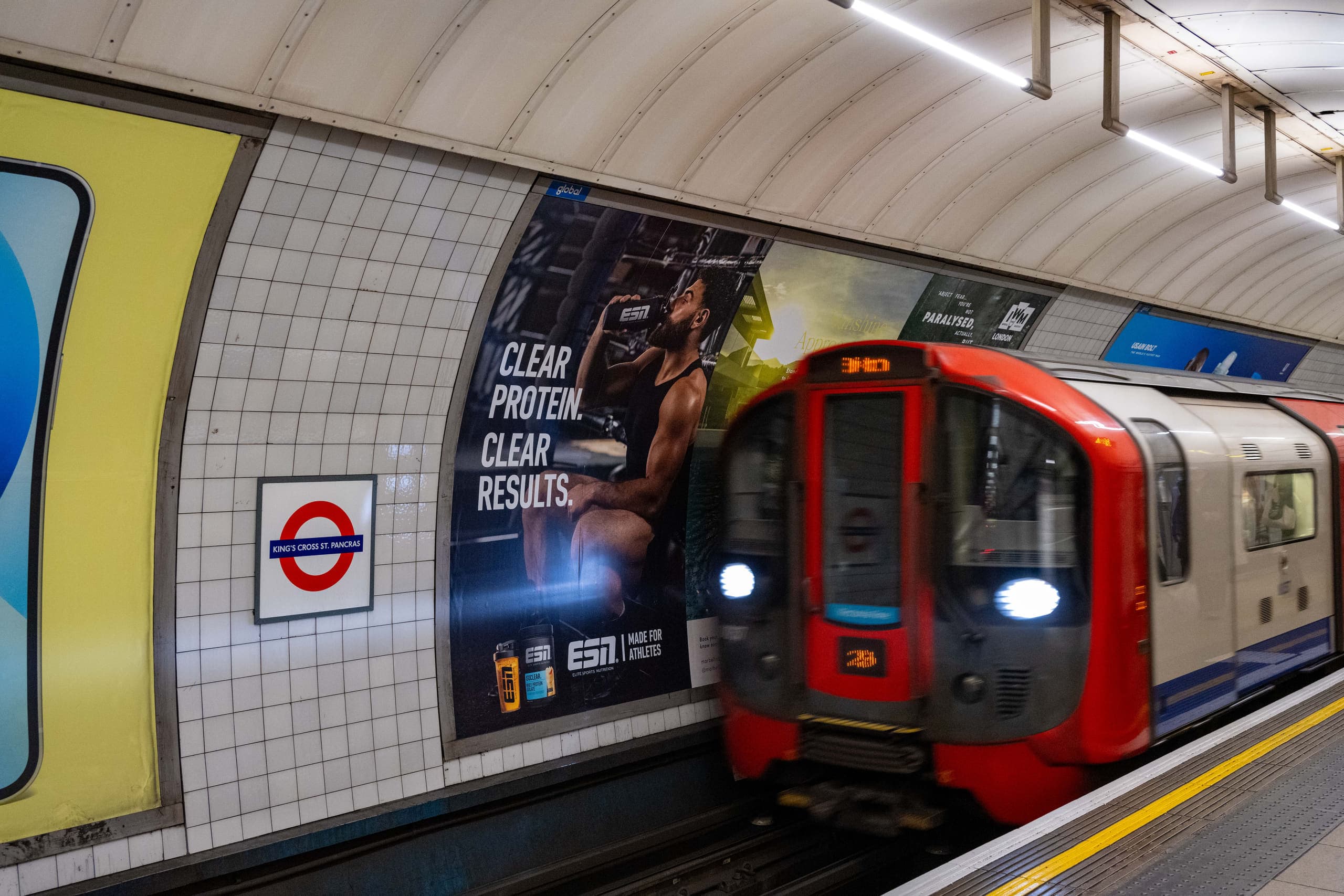 A cross-track 16-sheet poster advertising ESN on the platform wall at King's Cross St Pancras, with a Northern line train arriving.