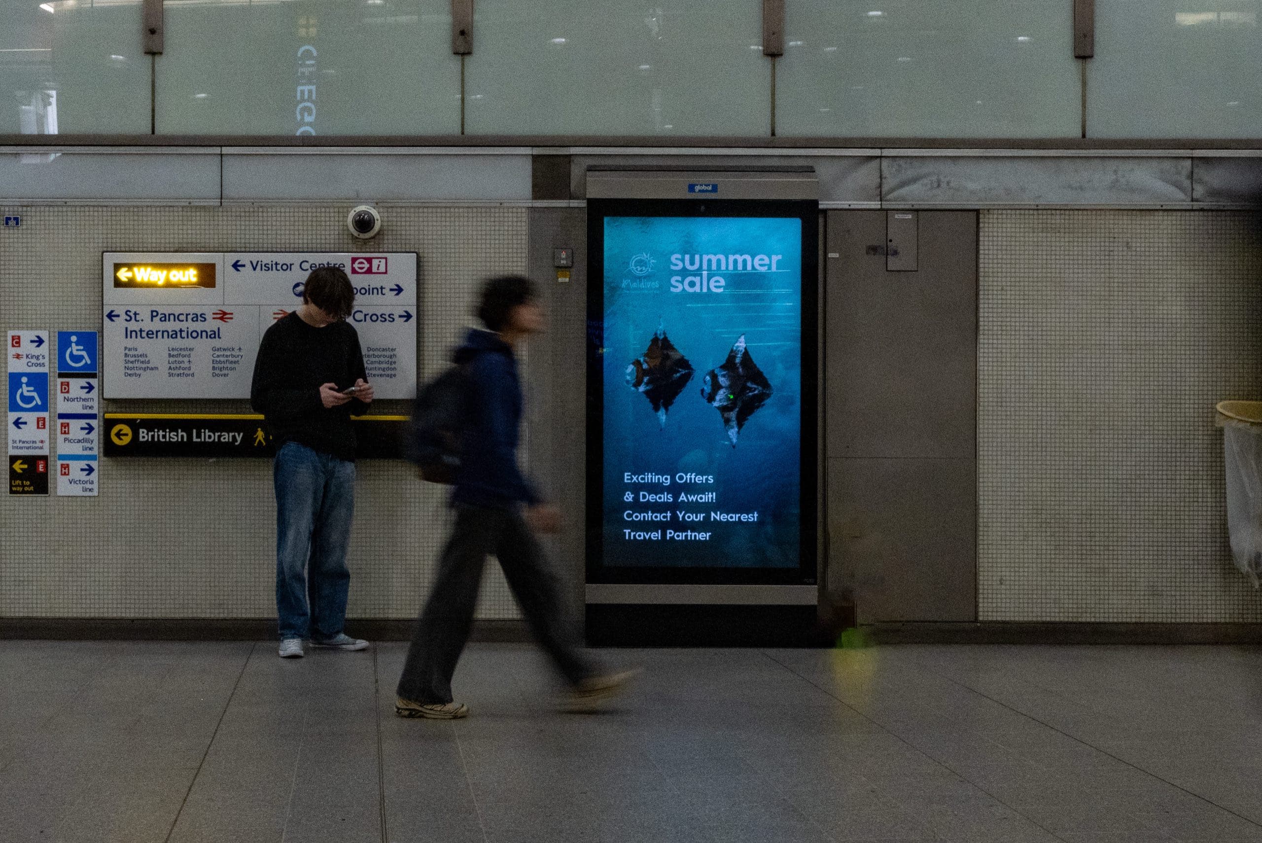 A second Visit Maldives execution on the same King’s Cross St Pancras digital screen, showing manta rays underwater beside the station wayfinding.