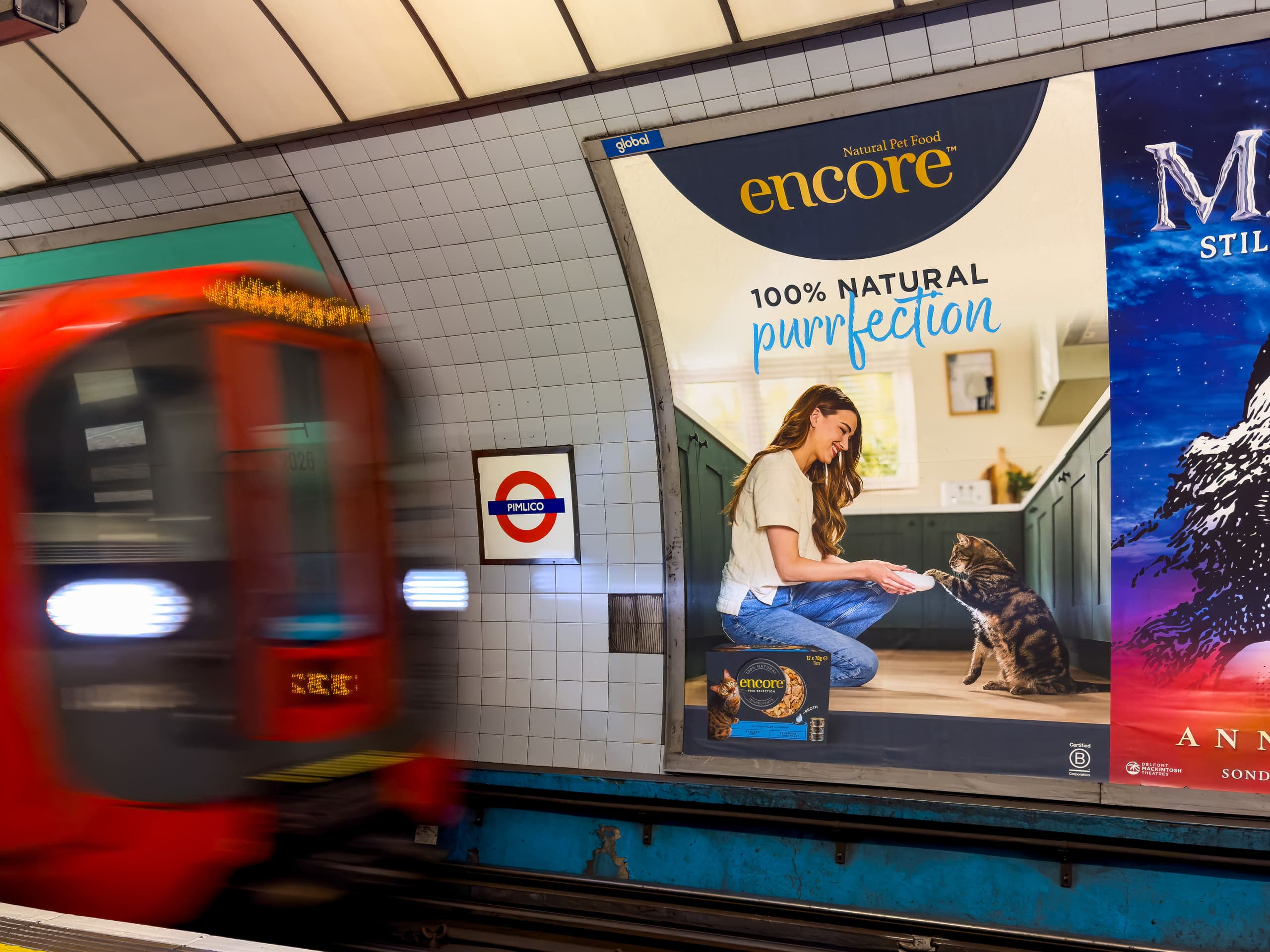 A cross-track poster advertising Encore on the tiled platform wall at Pimlico, with a train passing.