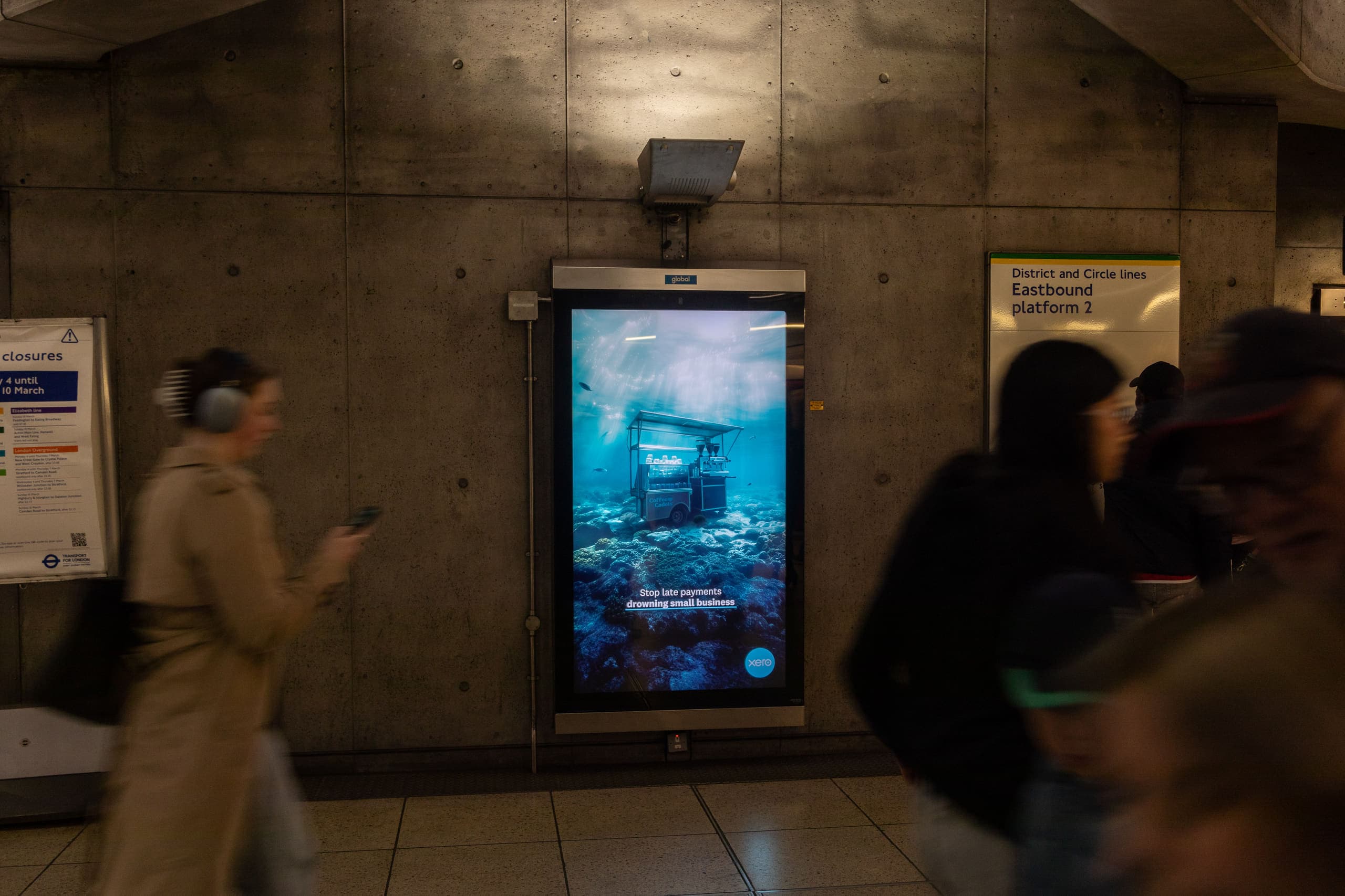 A digital 6-sheet screen carrying a Xero advertisement, mounted against the board-marked concrete of Westminster station beside the sign for the eastbound District and Circle line platform.